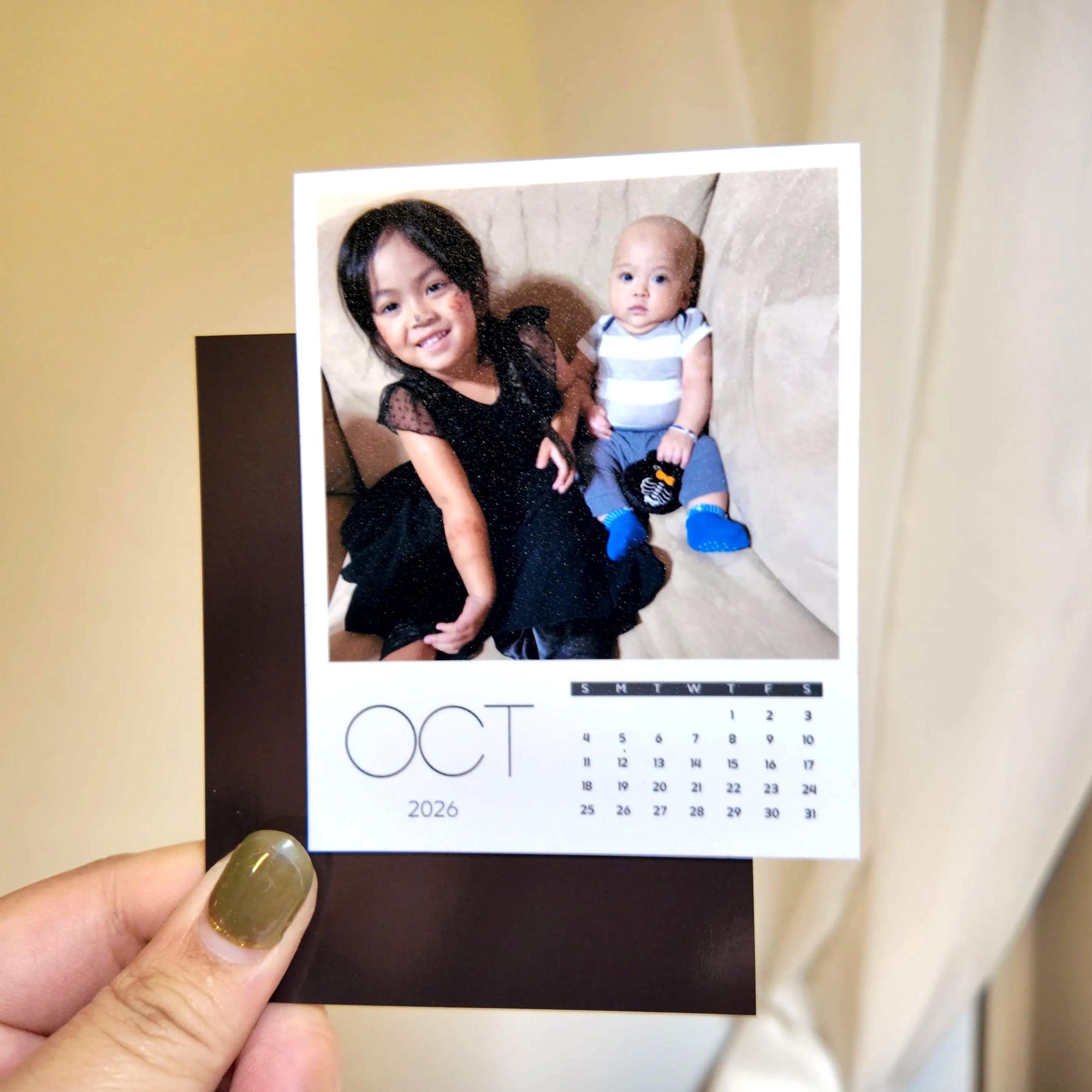A person is holding a small photo album with a photo of a young girl and a baby, along with a calendar for the month of October.
