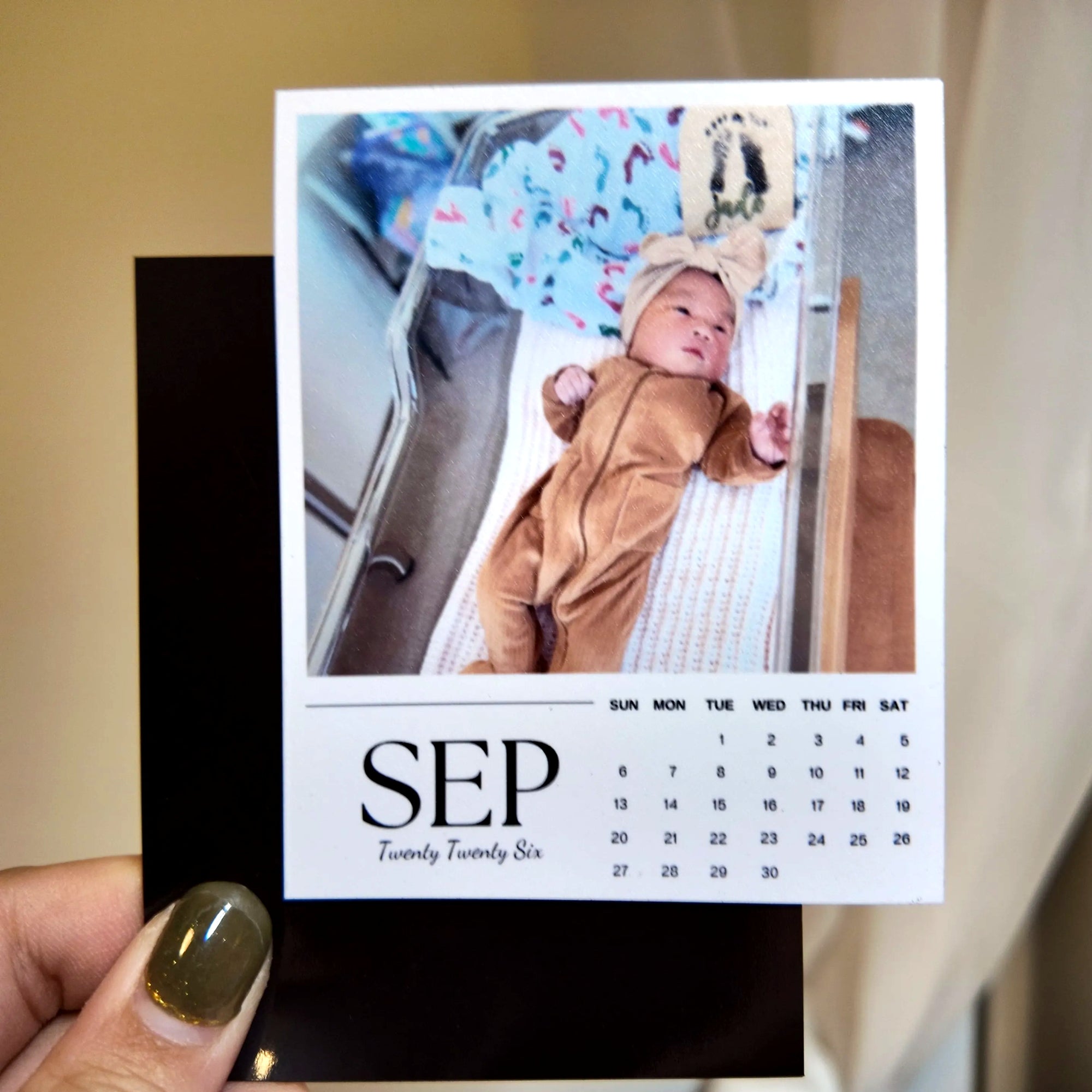 A person is holding a calendar featuring a photo of a baby in a crib.
