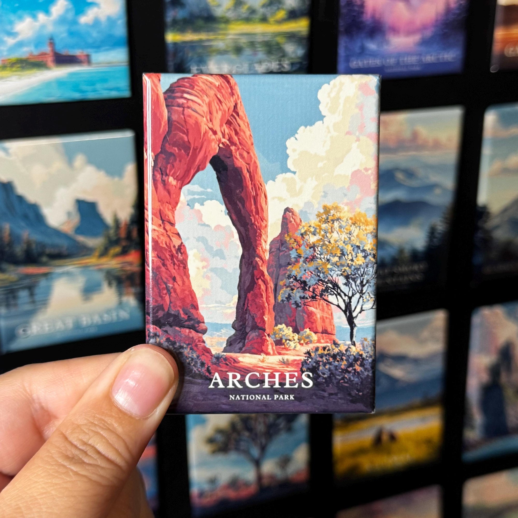 A hand holding a magnet with an illustration of a red rock formation, which appears to be the Arches National Park.