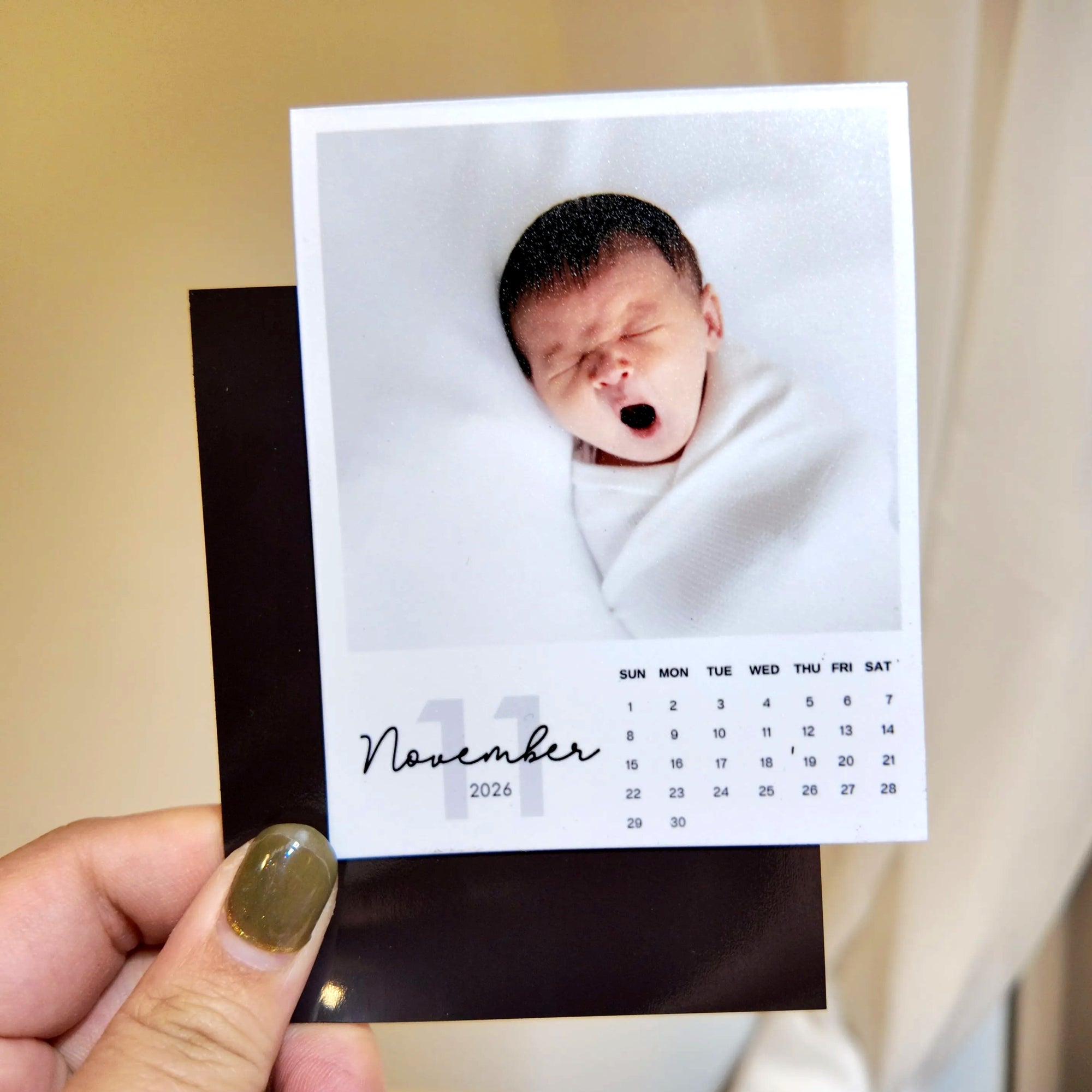 A person is holding a small calendar featuring a photo of a sleeping baby.