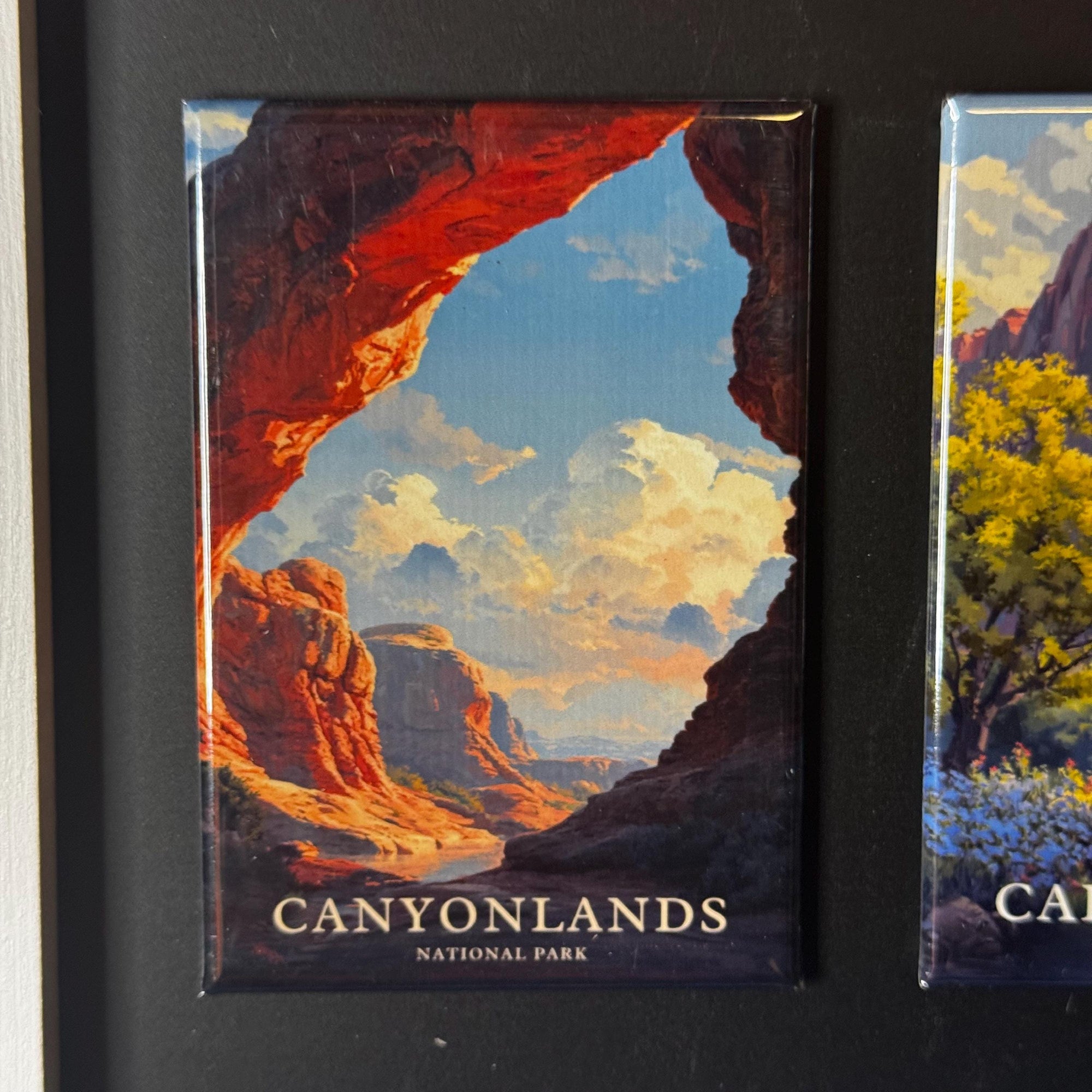 The image is a framed magnet depicting a scenic landscape with mountains, clouds, and a river.