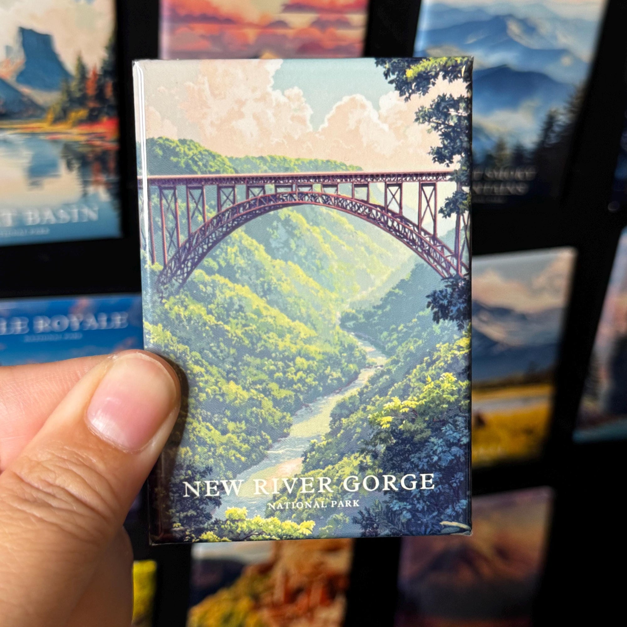 A hand holding a magnet with an illustration of a bridge over a river, surrounded by lush greenery.
