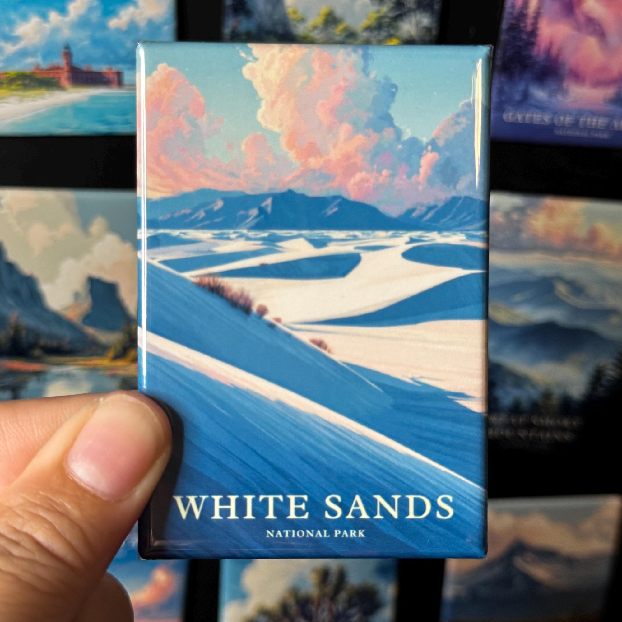 A hand holding a magnet with a landscape image of the White Sands National Park.