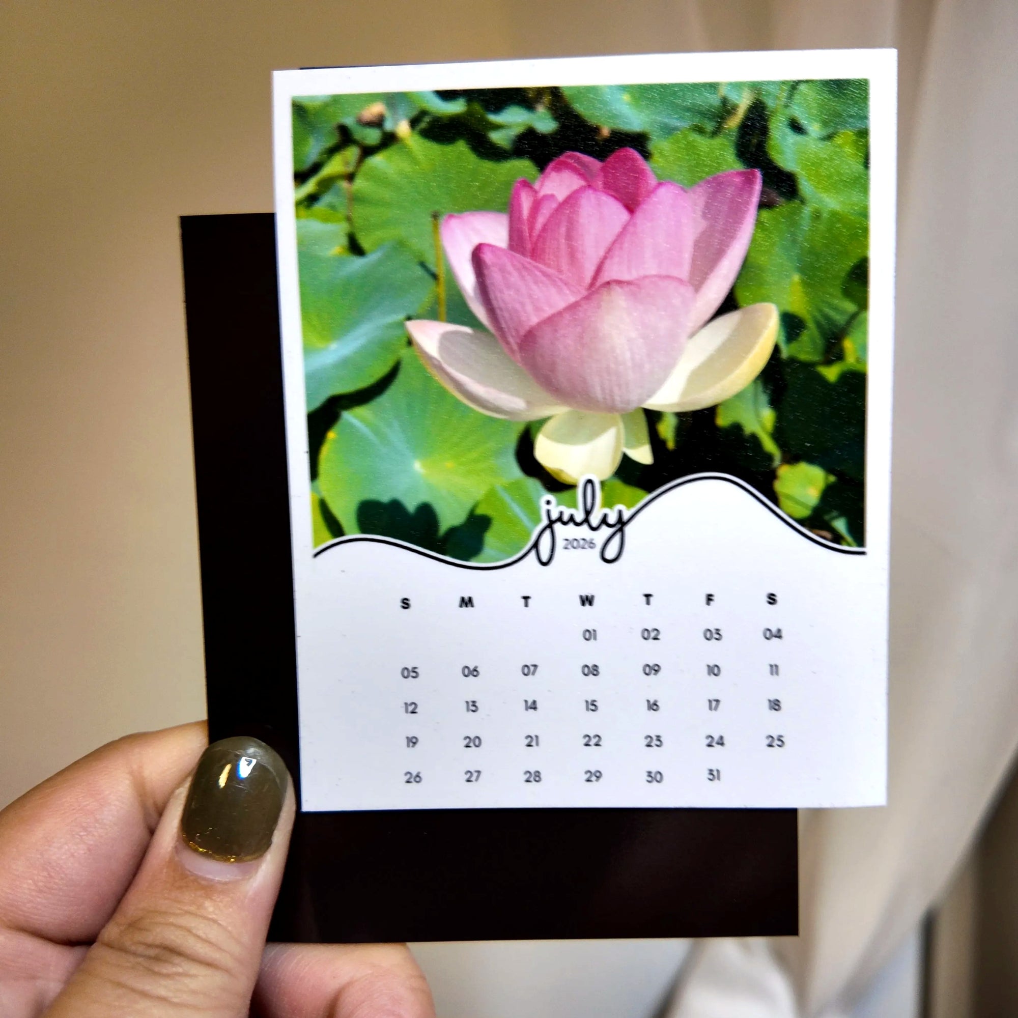 A hand holding a small calendar with a pink flower image on the cover.