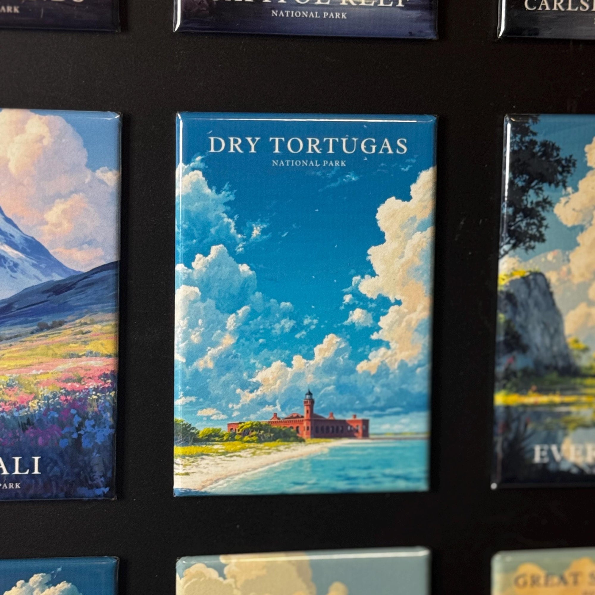 a collection of magnets depicting various scenes, including a beach, mountains, and a lighthouse. The magnets are arranged in a grid-like pattern, with the central one being the focal point.
