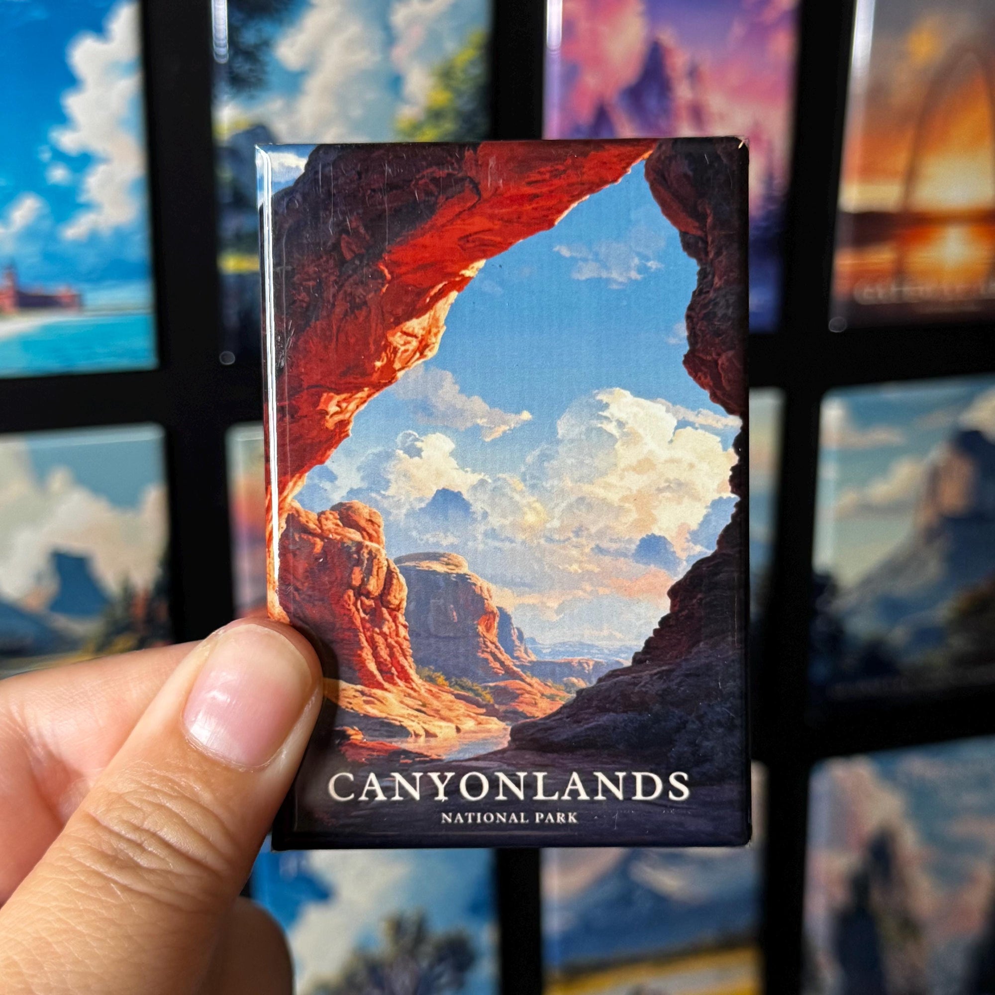 A hand holding a magnet with a picture of a canyon landscape, with the text "CANYONLANDS NATIONAL PARK" visible.