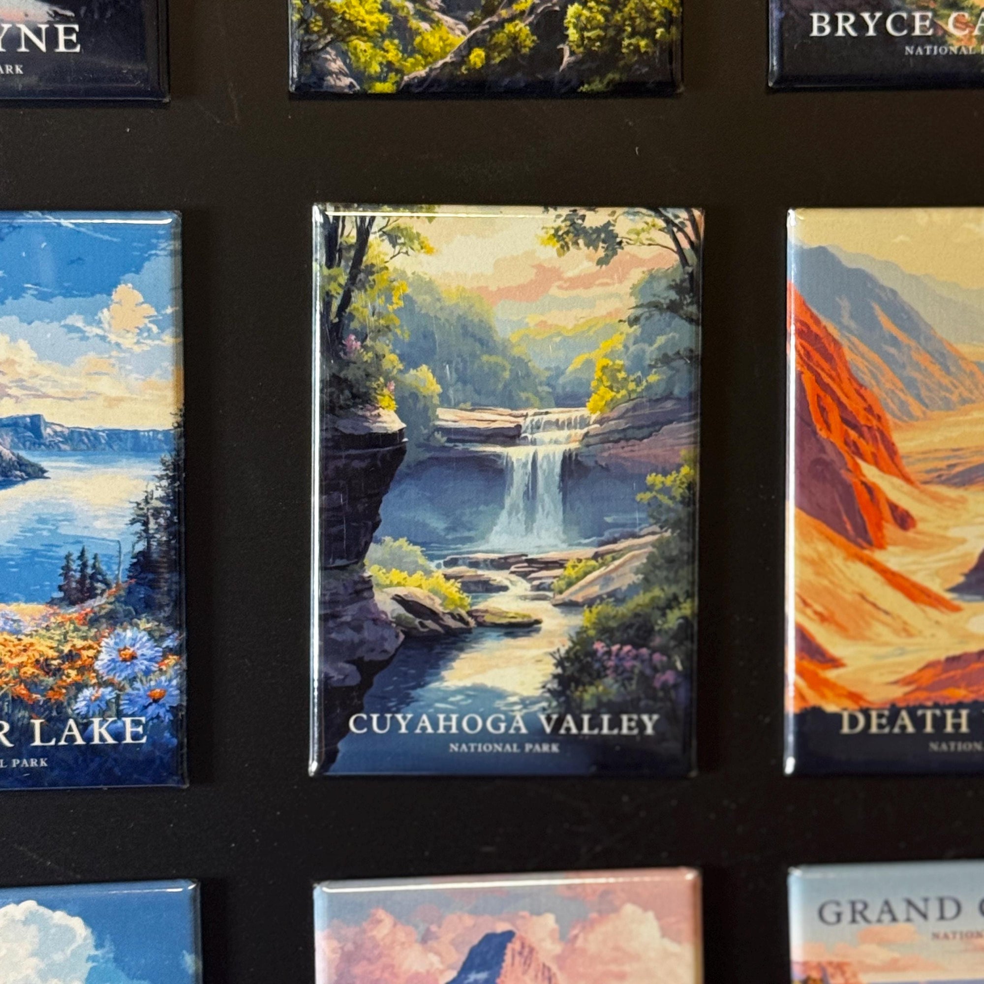 a collection of landscape magnets, each depicting a different natural scene. The magnets are arranged in a grid-like pattern, showcasing various pictures of national parks, including Cuyahoga Valley National Park and Grand Canyon National Park.
