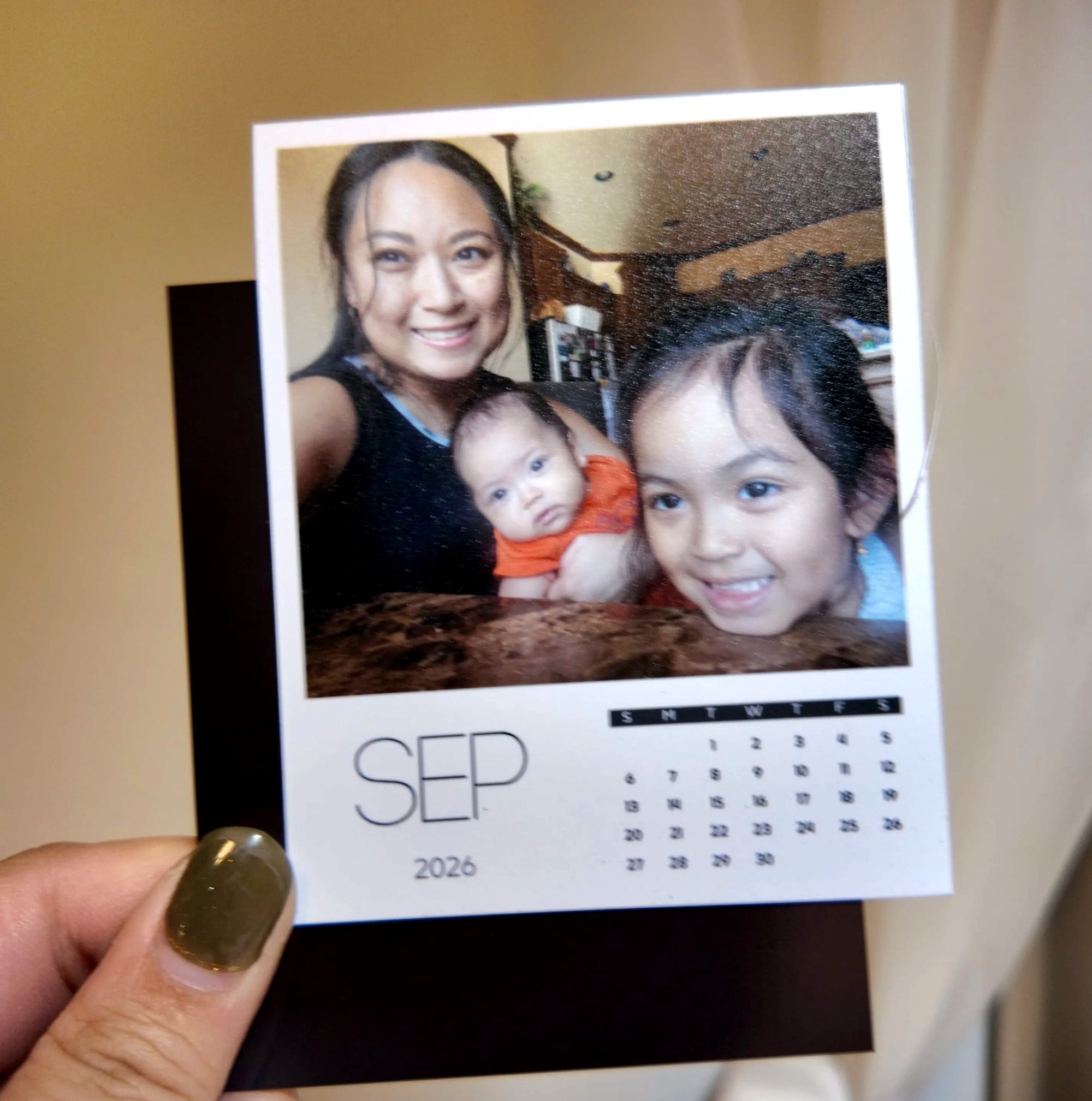 A person is holding a small photo album with a photo of a woman and two children, and a calendar for the month of September.