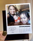 A person is holding a small photo album with a photo of a woman and two children, and a calendar for the month of September.
