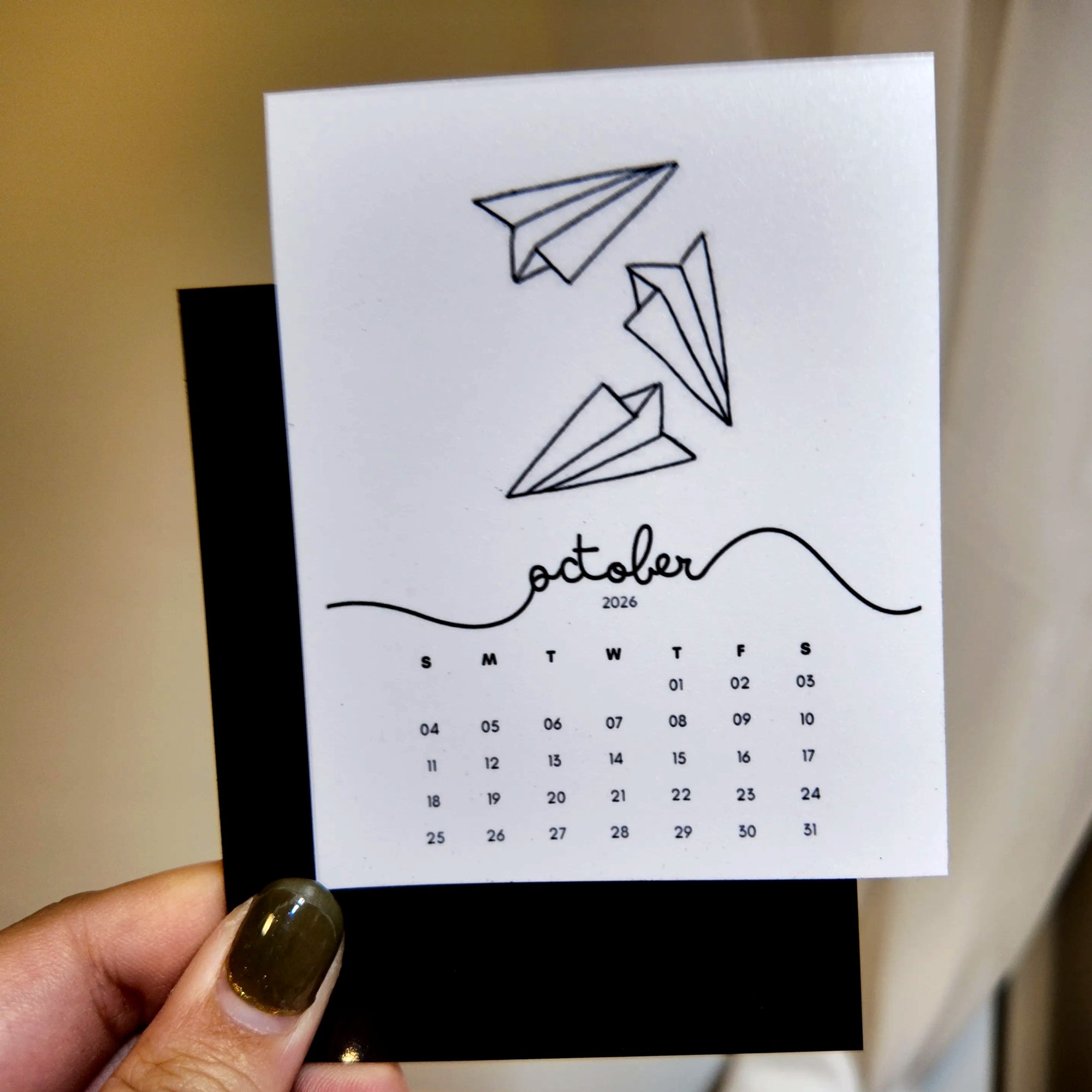 A person is holding a calendar card with a simple design of paper airplanes on it.