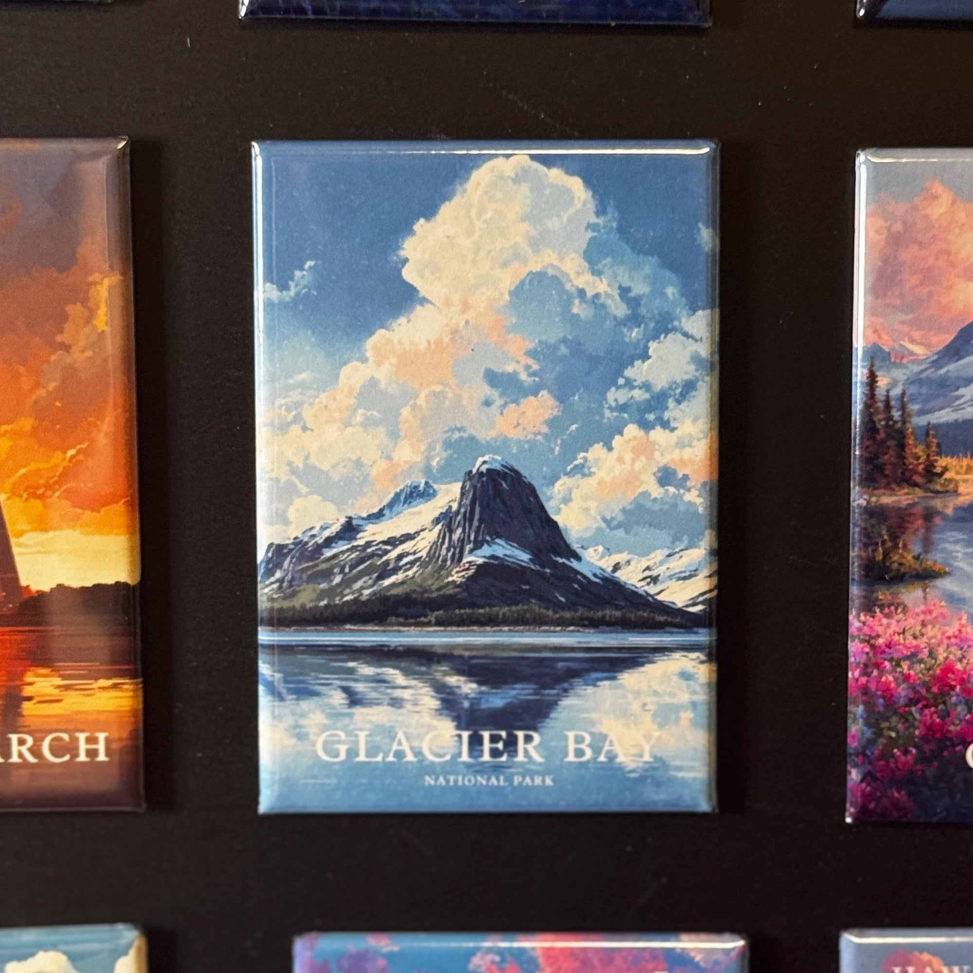 a collection of magnets depicting various landscapes, including a mountain range, a lake, and a sunset. The magnets are arranged in a row, showcasing the beauty of these natural scenes.