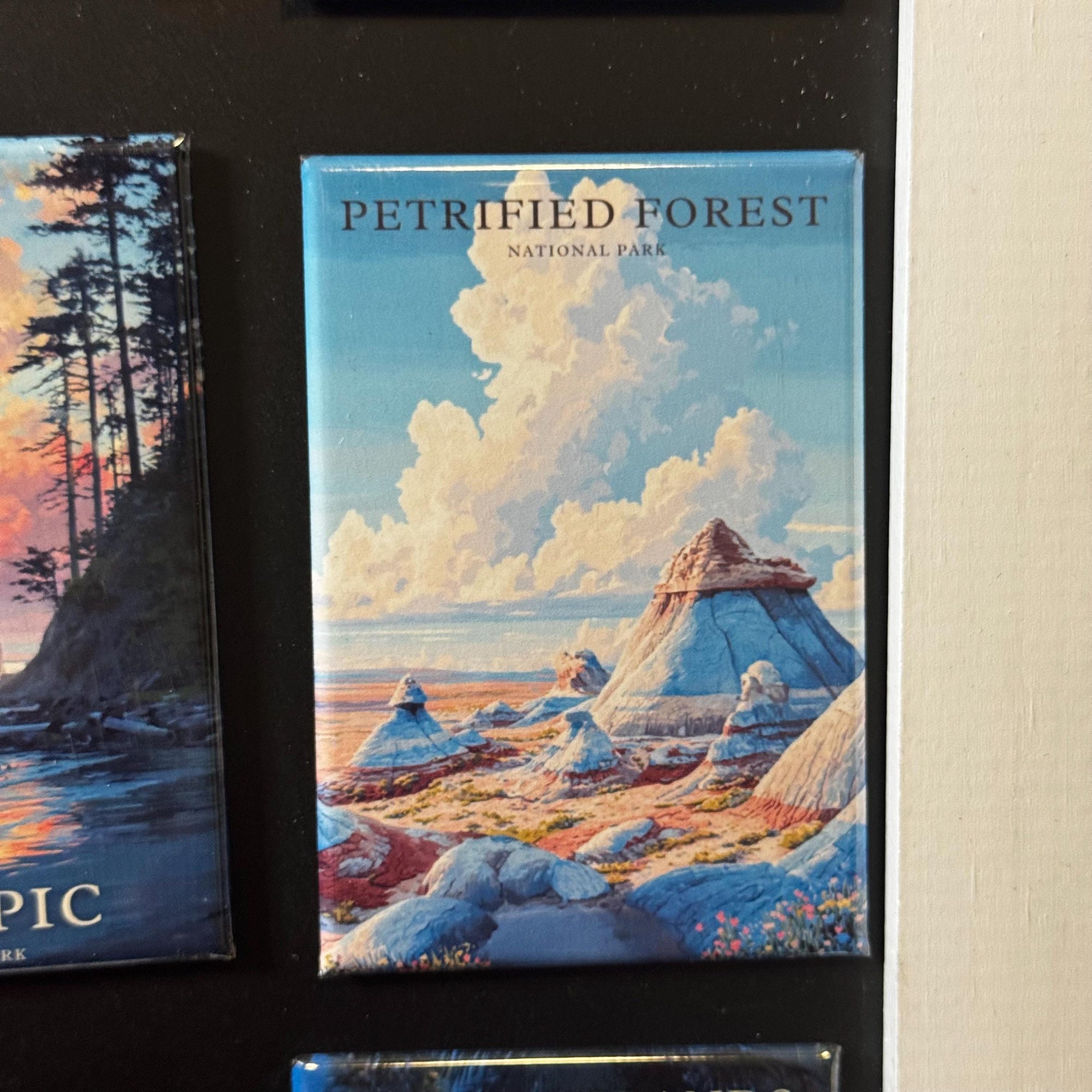 a large magnet with a painting of a forest landscape, including mountains, trees, and a cloudy sky.