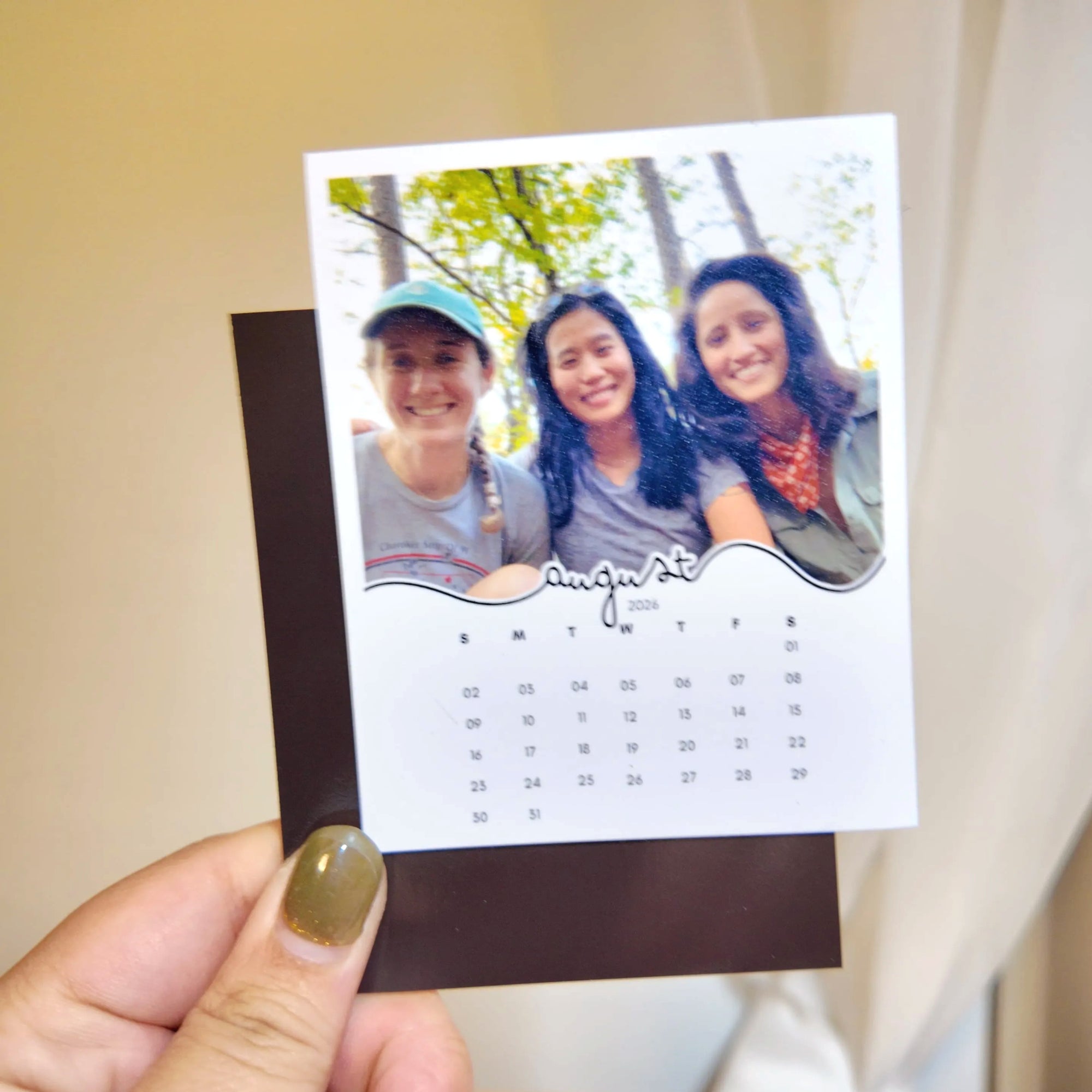 A person is holding a small photo frame with a photo of three smiling women inside it.