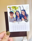 A person is holding a small photo frame with a photo of three smiling women inside it.