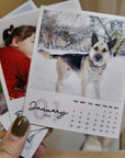 A hand holding a small, square-shaped photo album with a dog image on the cover, and a calendar for the month of January for the year 2026.