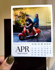 A hand holding a calendar page with a photo of two people on a red scooter.