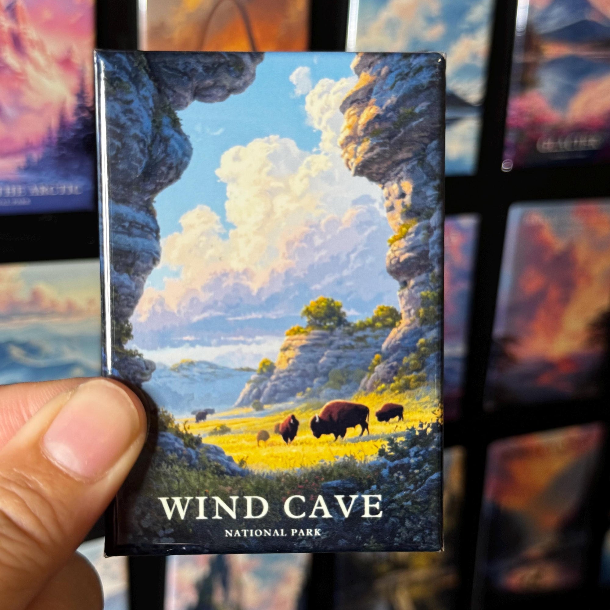A hand holding a magnet with a landscape scene depicting a wind cave and bison in the background.