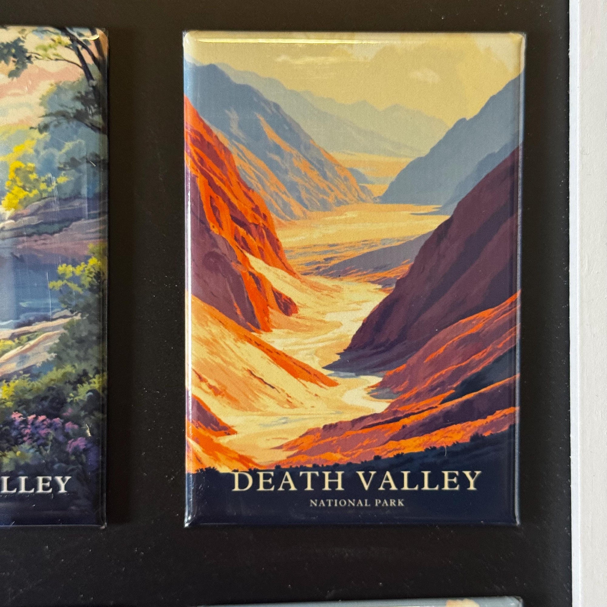 The image is a framed magnet depicting a scenic view of Death Valley National Park, with mountains, valleys, and a river flowing through the landscape.