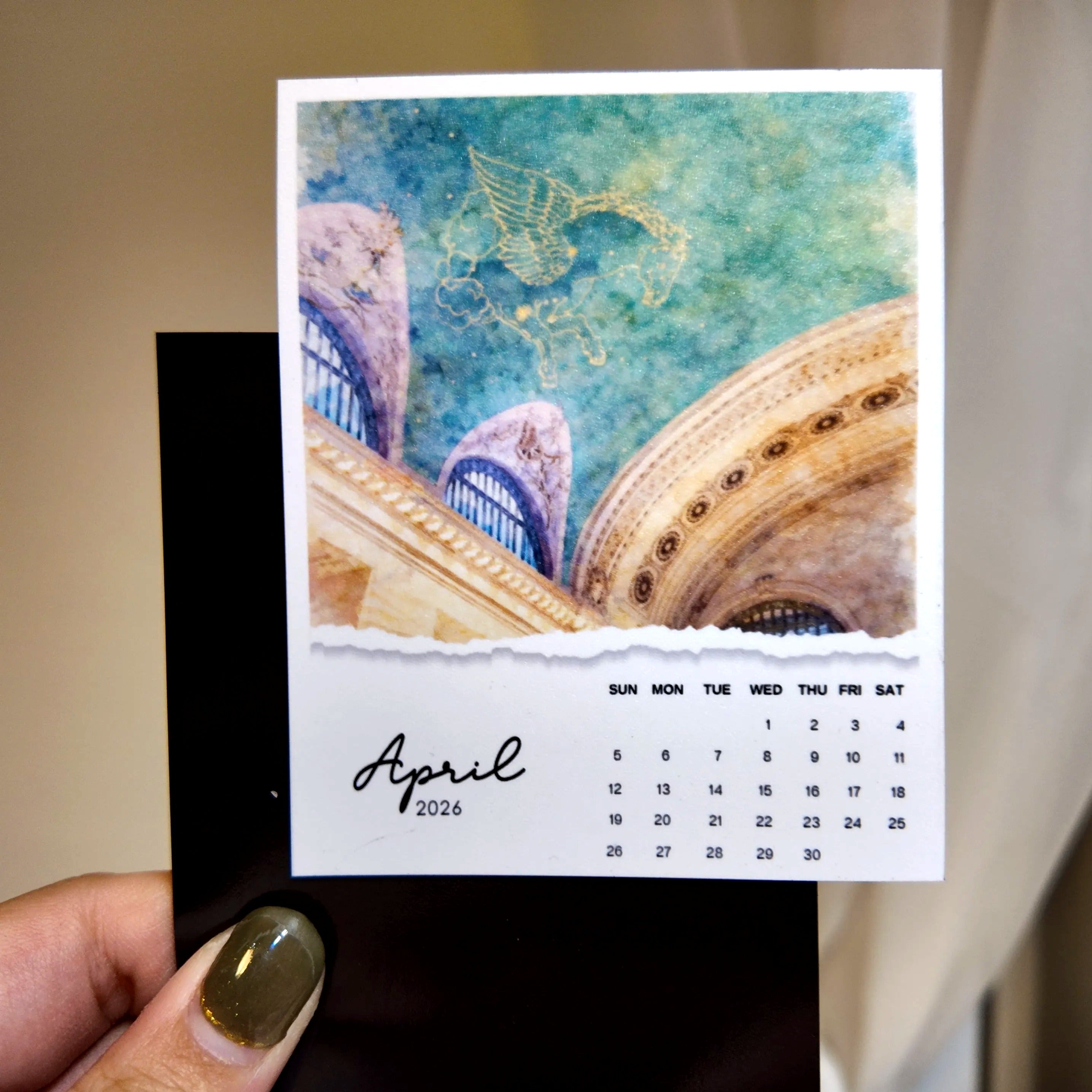 A hand holding a small calendar with a picture of a building and a bird on the cover, and a calendar for the month of April.
