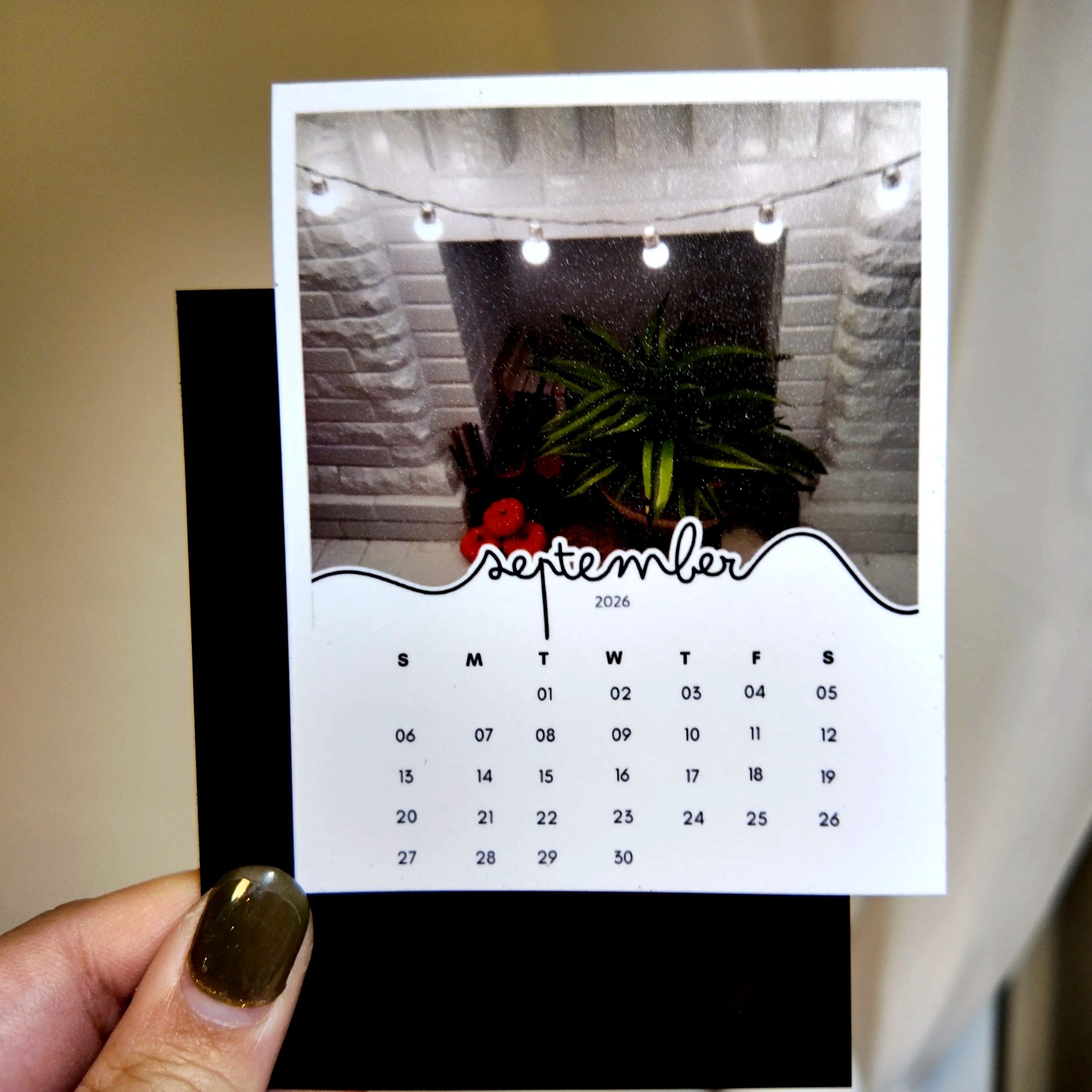 A person is holding a calendar card with a photo of a fireplace and a plant on it.