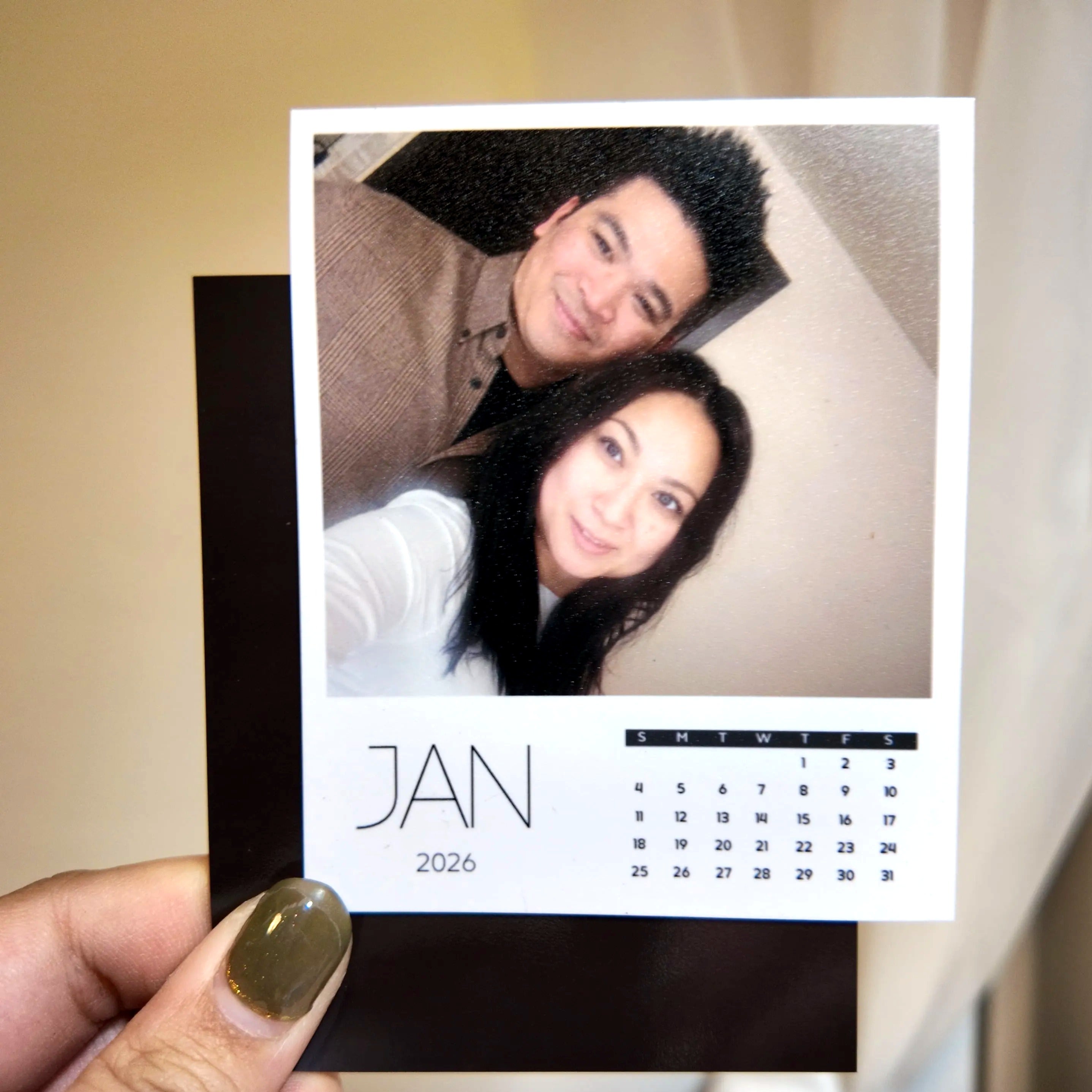 A person is holding a small square photo frame containing a photo of a man and a woman, along with a calendar for the month of January.
