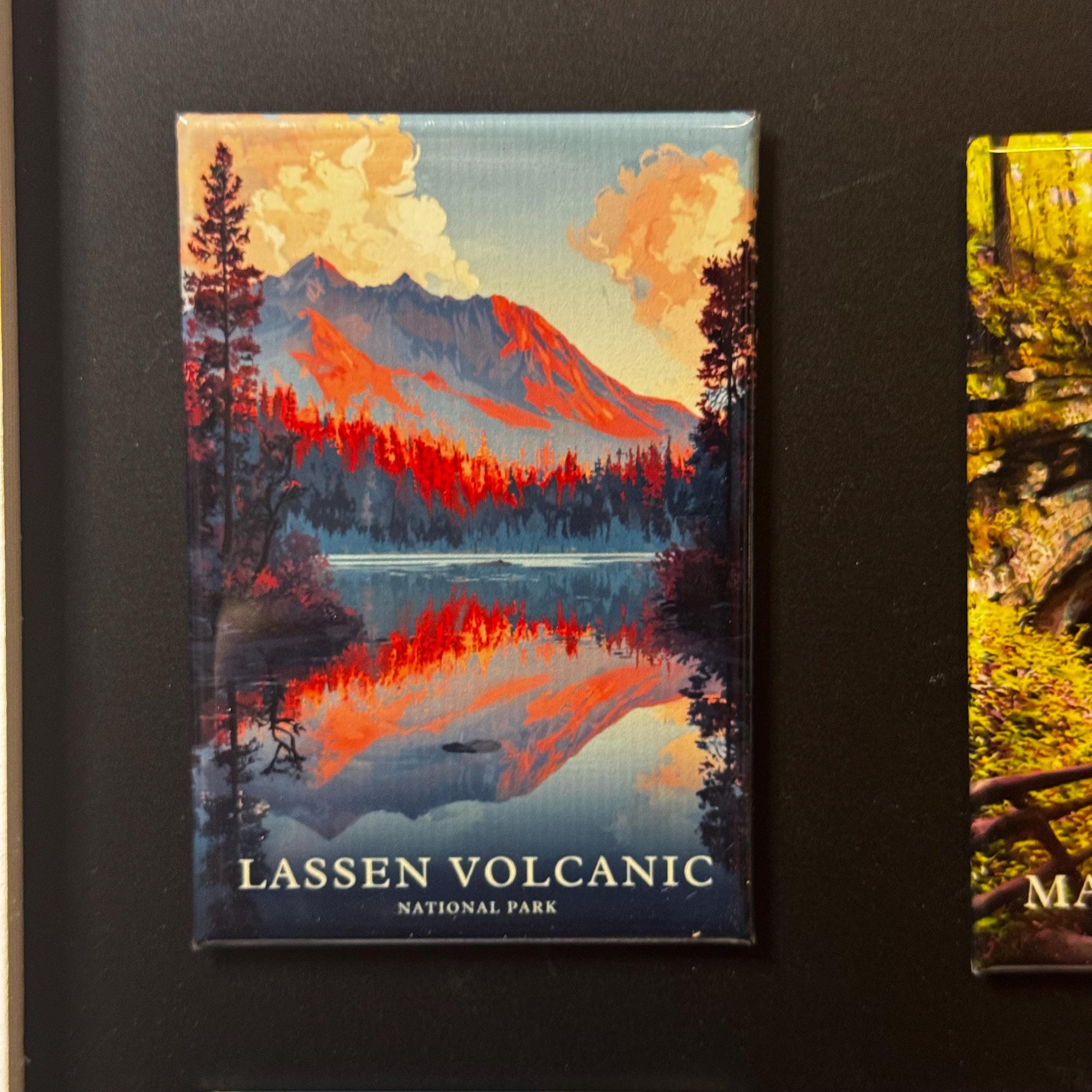 A framed magnet depicting a scenic landscape with a lake and mountains, with the text "LASSEN VOLCANIC NATIONAL PARK" printed on it.
