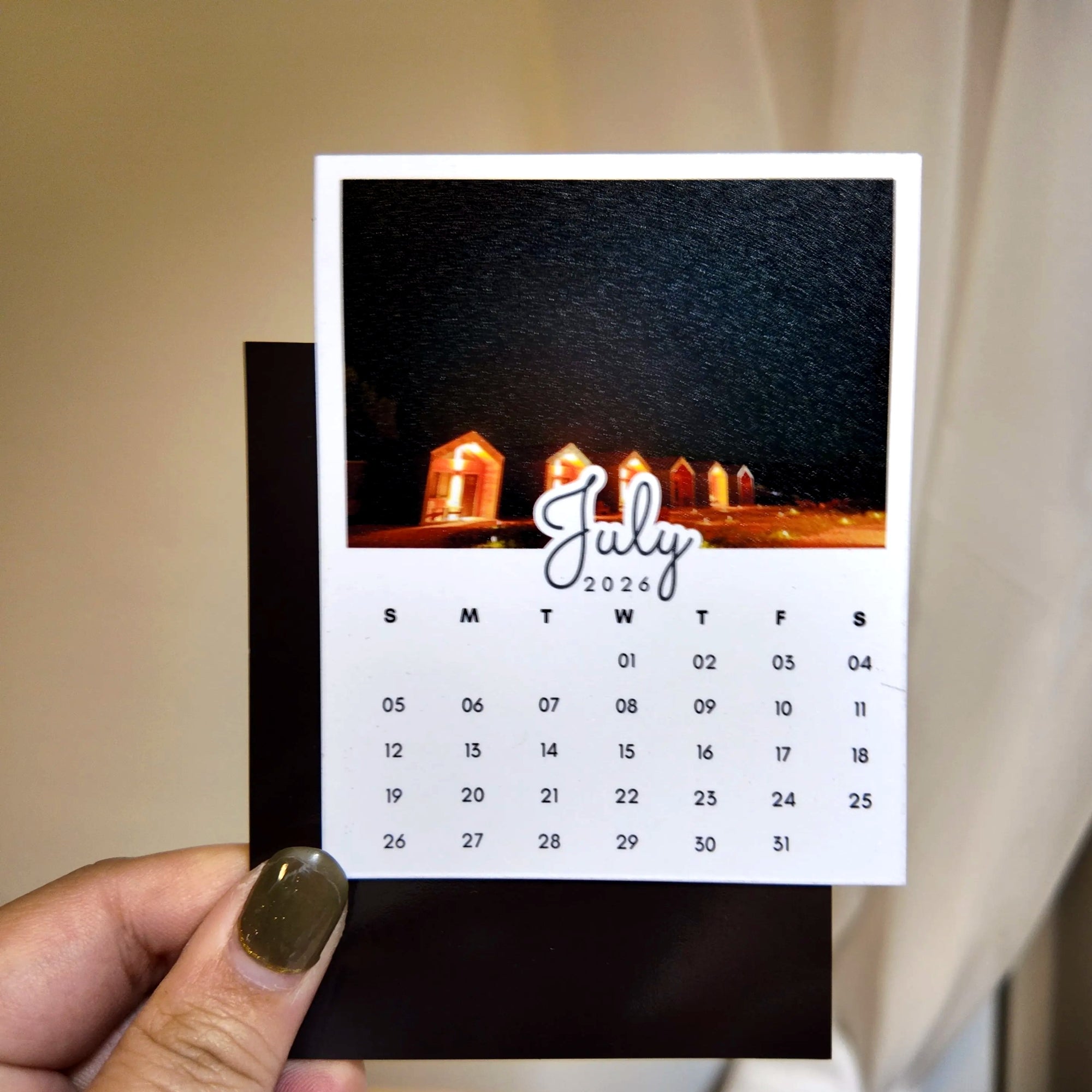 A hand holding a small calendar card with a photo of a building at night on it.