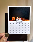 A hand holding a small calendar card with a photo of a building at night on it.
