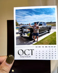 A person holding a calendar card with a photo of a man standing next to a truck.