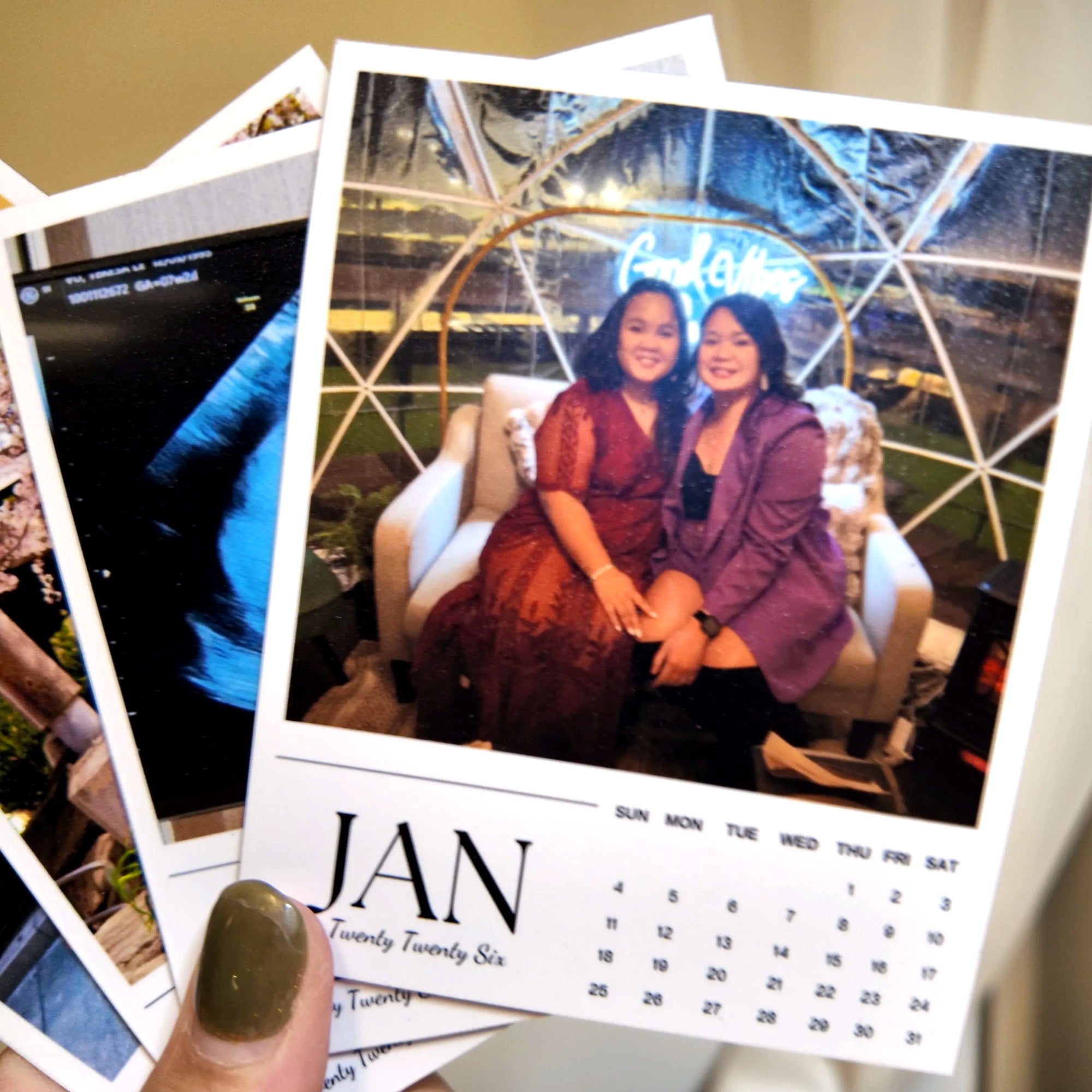 A person's hand holding a calendar with a photo of two women sitting together, with a neon sign visible in the background.