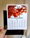 A person's hand holding a small calendar card with a photo of a tree on the cover.