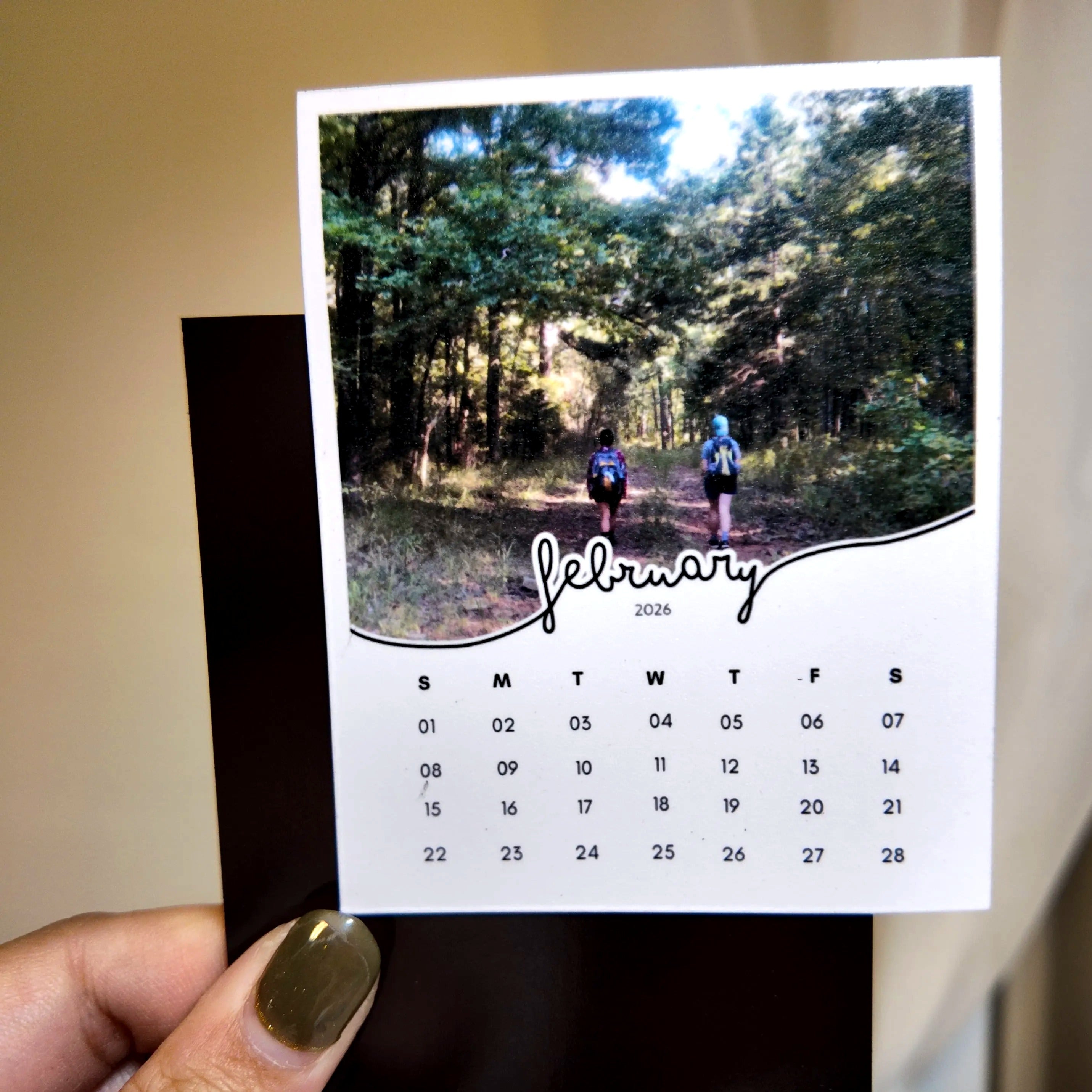 A person is holding a calendar featuring a photo of two people walking on a path through a forest.