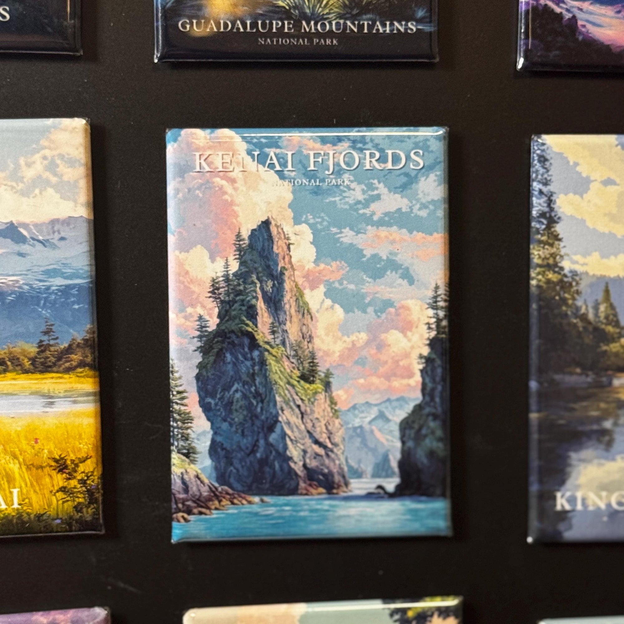 a collection of landscape magnets, including one with a mountain and a body of water, as well as another with a forest and a mountain.