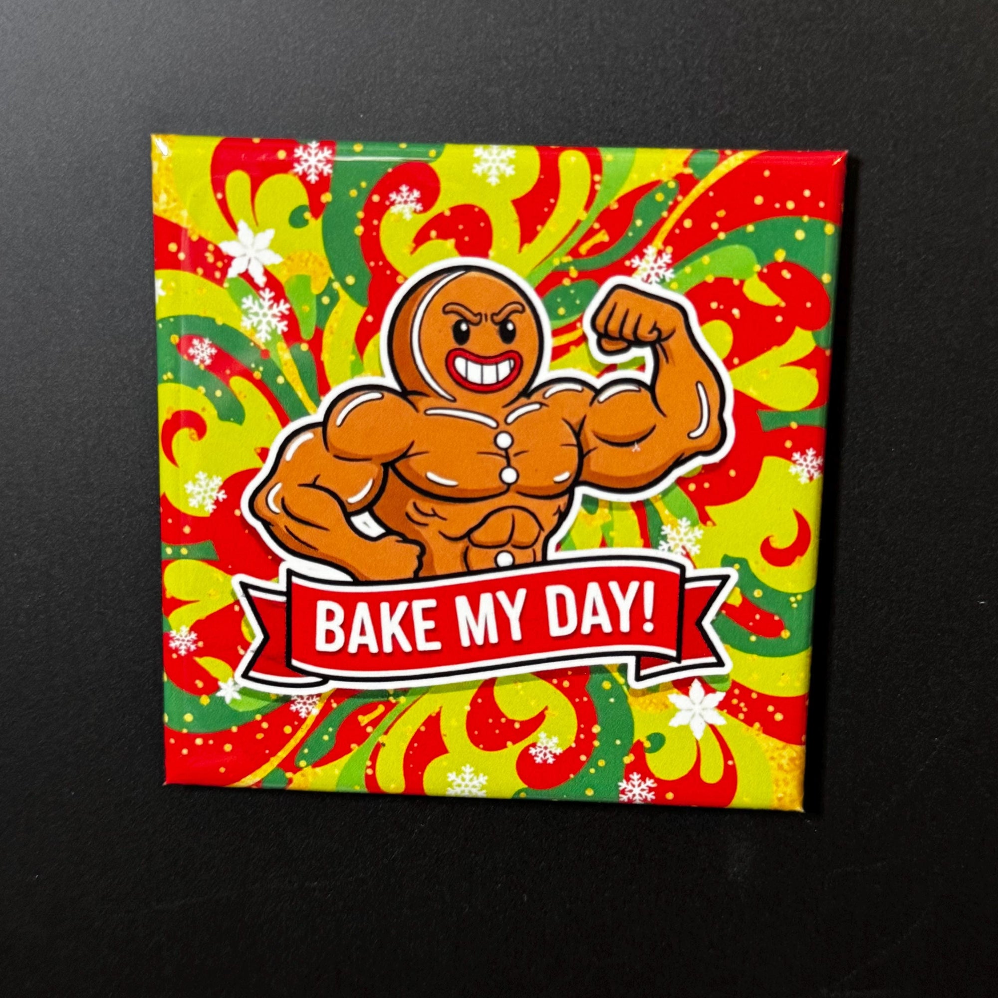A muscular gingerbread man with a flexed arm, wearing a red and yellow striped shirt, and the text "Bake My Day!" is displayed on a colorful background.