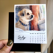A hand holding a small calendar featuring a dog image and the date "July 2026".