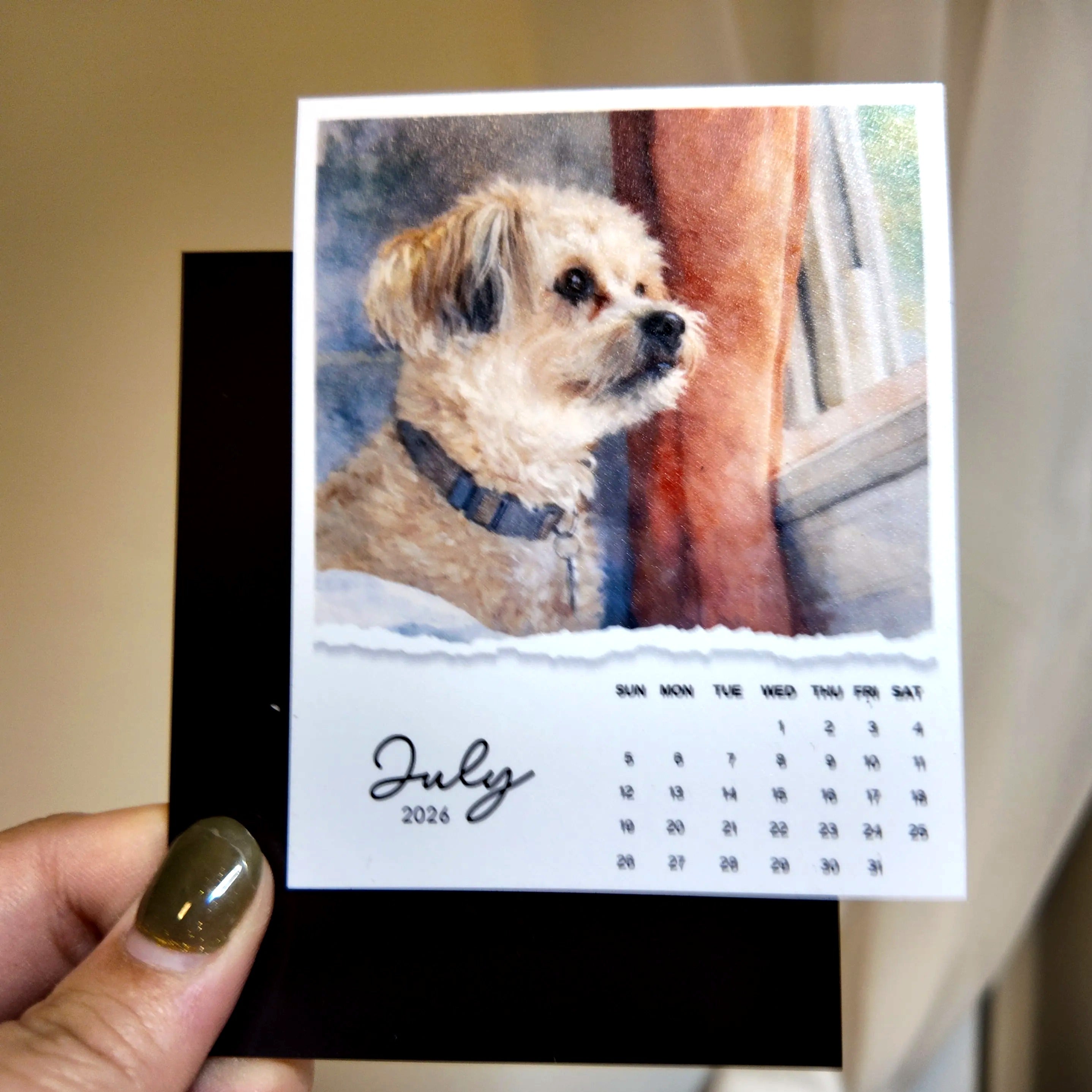 A hand holding a small calendar featuring a dog image and the date "July 2026".