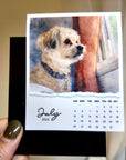 A hand holding a small calendar featuring a dog image and the date "July 2026".