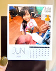 A person holding a photo of a young girl and a baby, with a calendar for the month of June visible.
