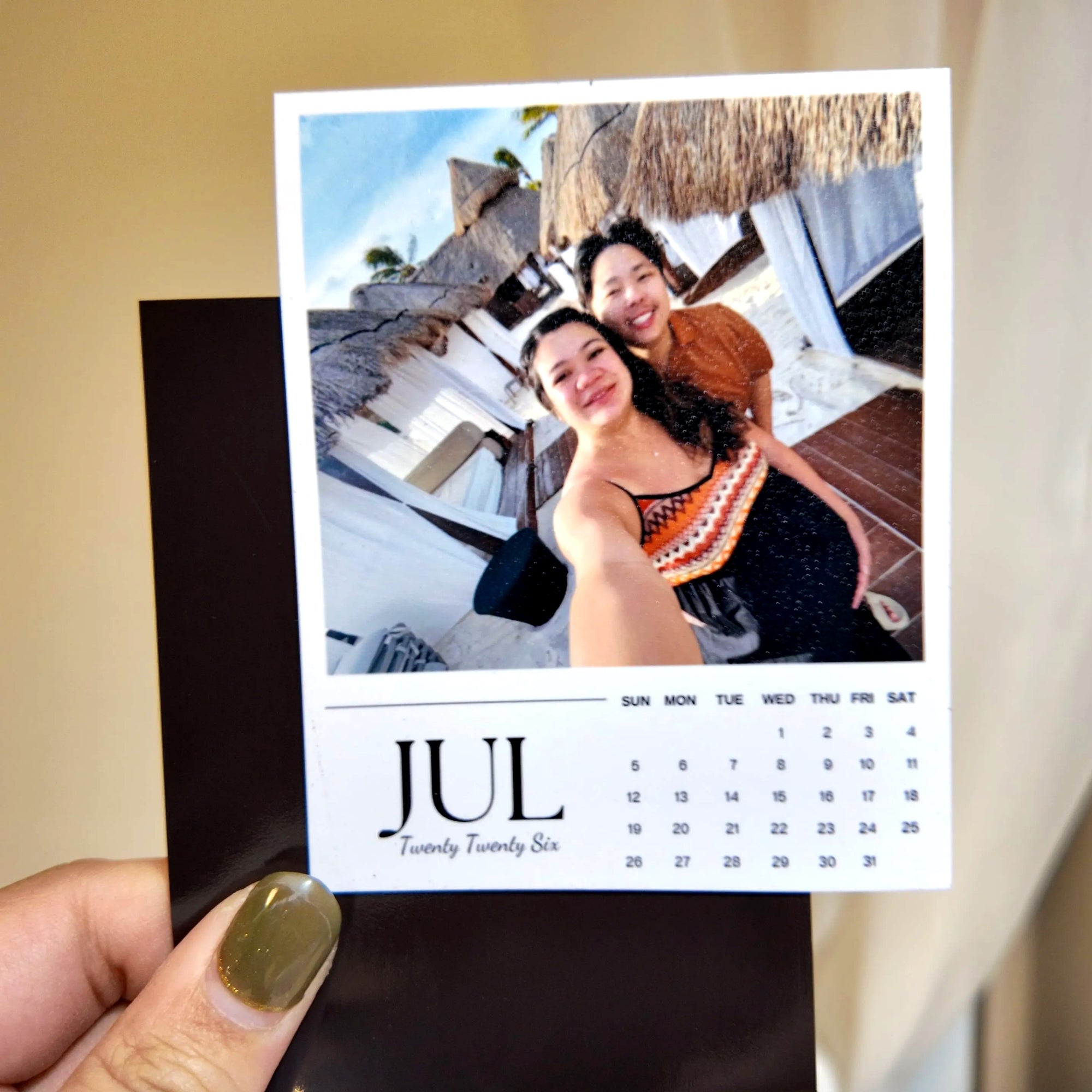A person is holding a small calendar card with a photo of two smiling women on it.