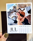 A person is holding a small calendar card with a photo of two smiling women on it.