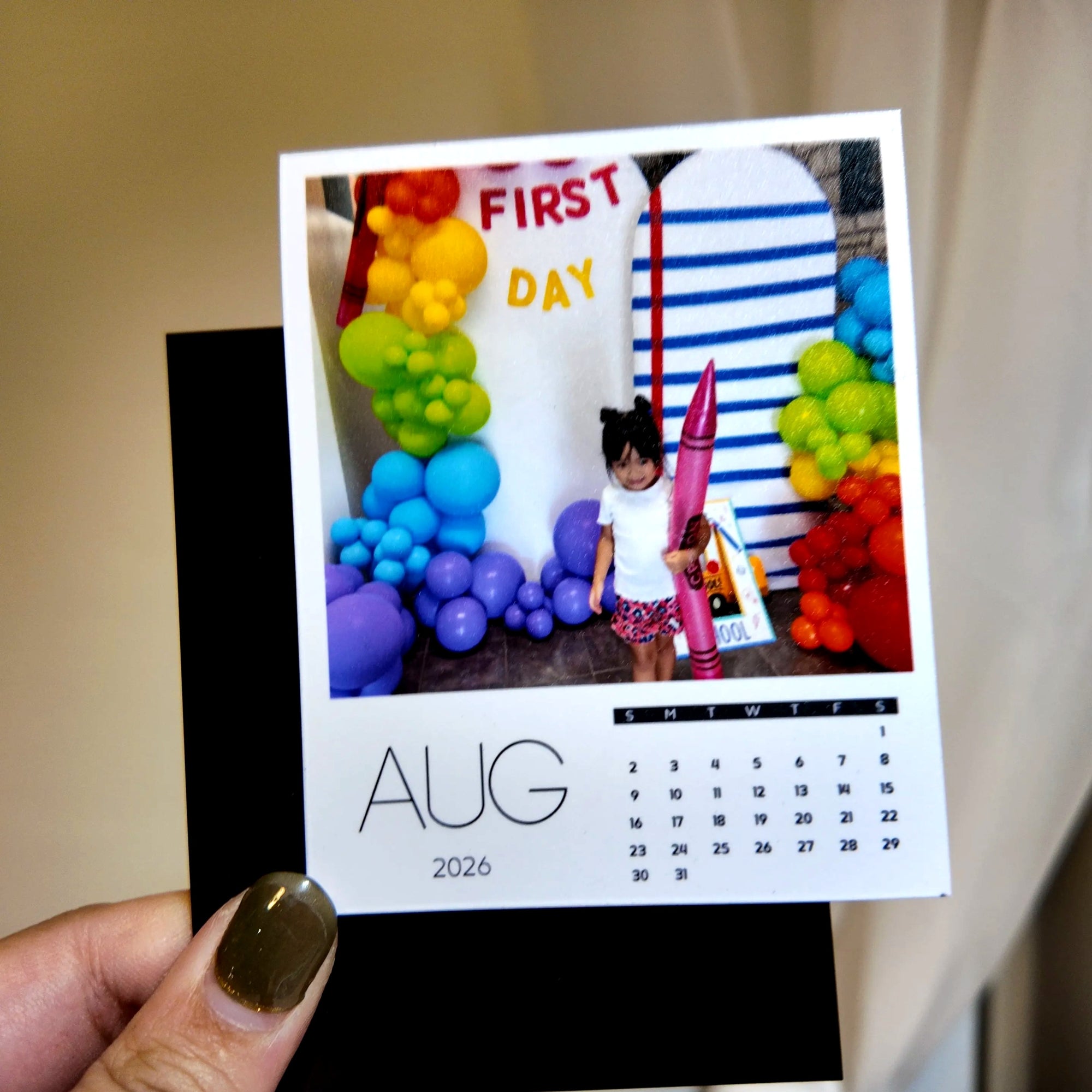 A person is holding a small calendar with a photo of a young girl standing in front of a colorful balloon arch.