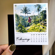 A person holding a calendar featuring a tropical beach scene with palm trees and a person in a red dress.
