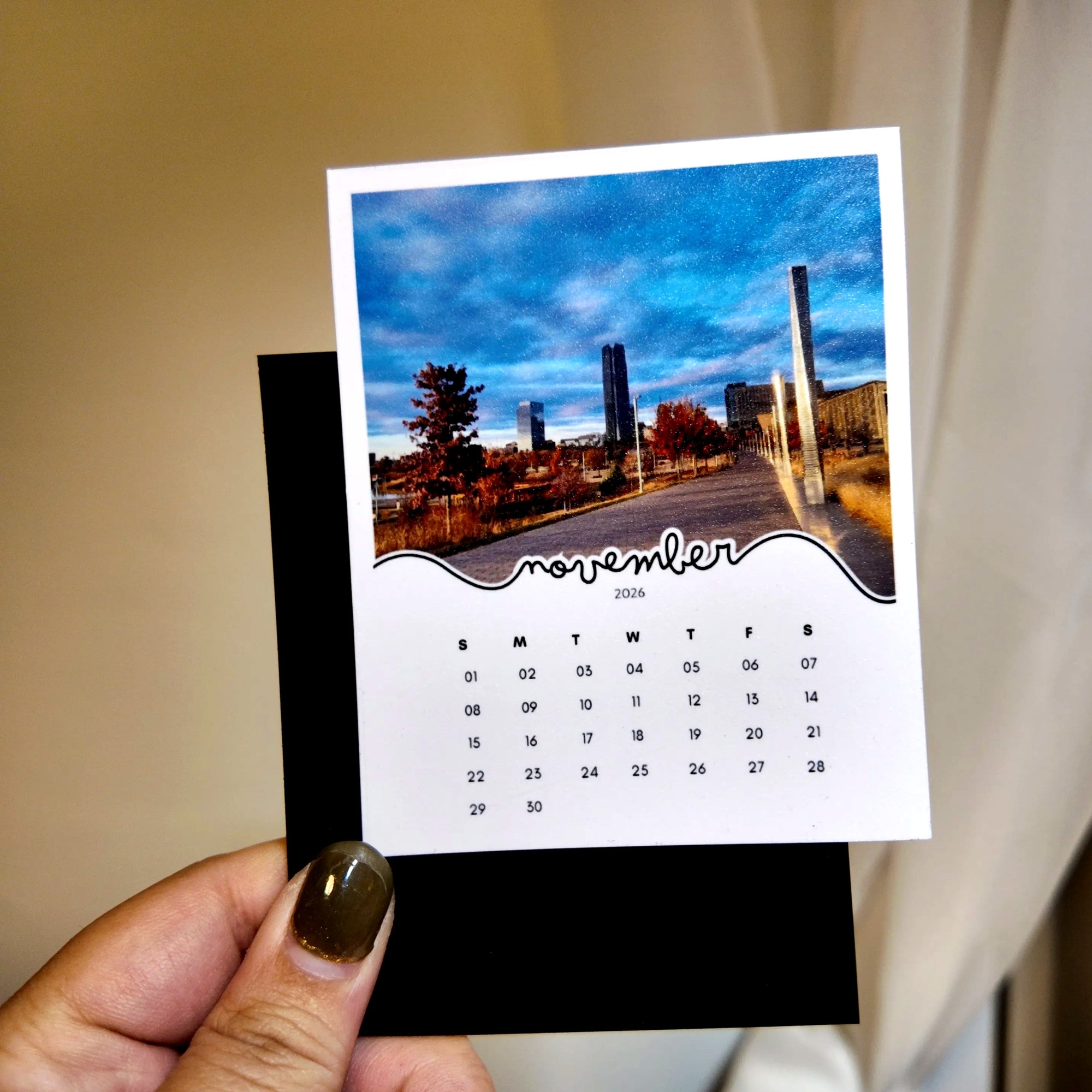 A person's hand holding a small calendar card with a photo of a city street and buildings.