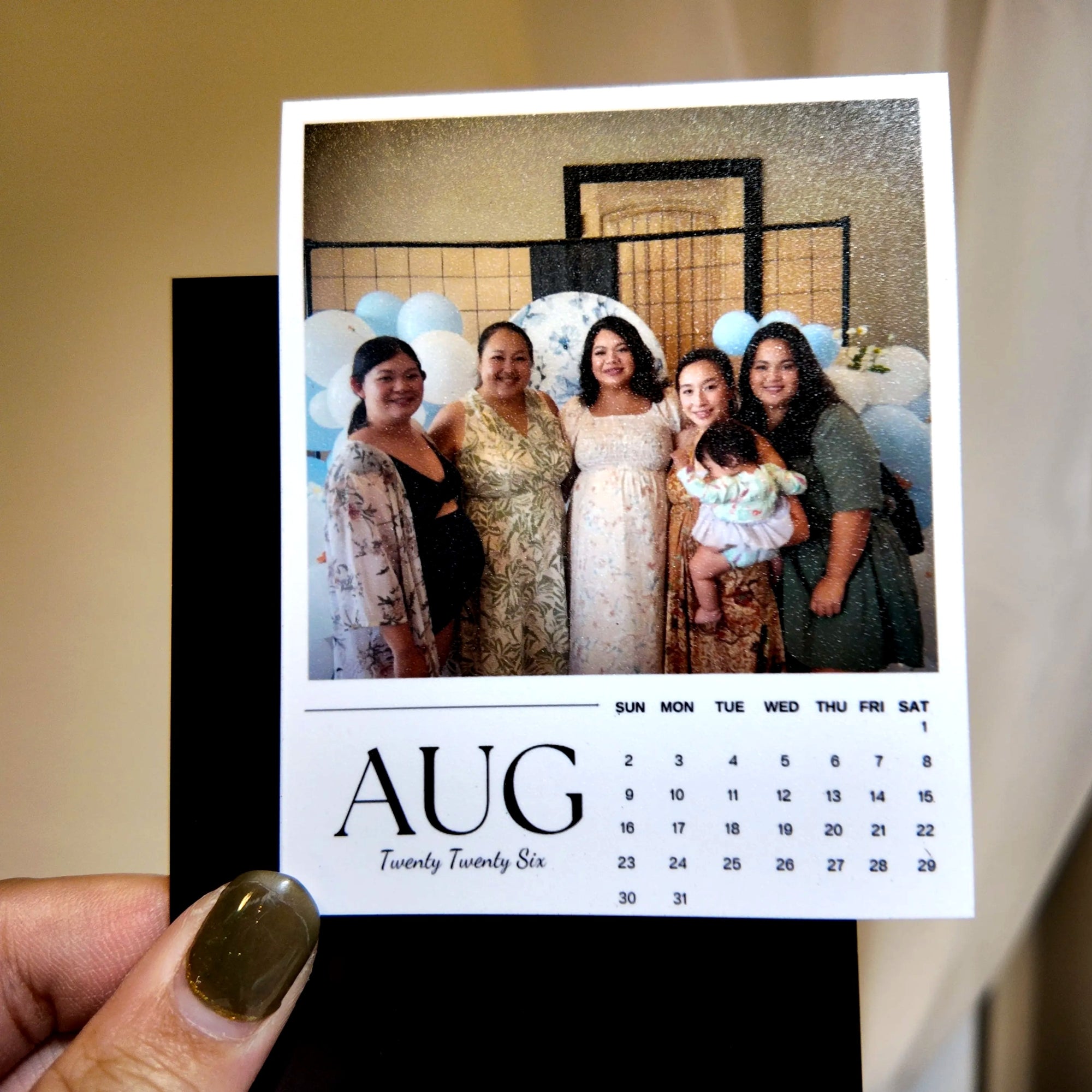 A hand holding a small calendar page with a photo of five smiling women posing together.