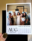 A hand holding a small calendar page with a photo of five smiling women posing together.