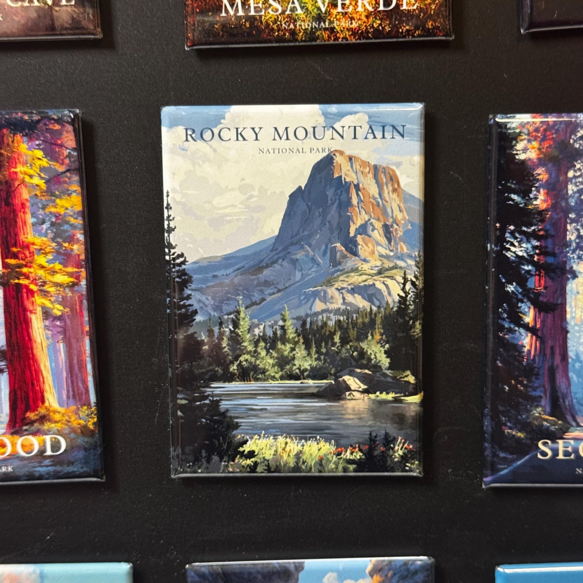 a large magnet with a scenic landscape of Rocky Mountain National Park, including a mountain, trees, and a lake.