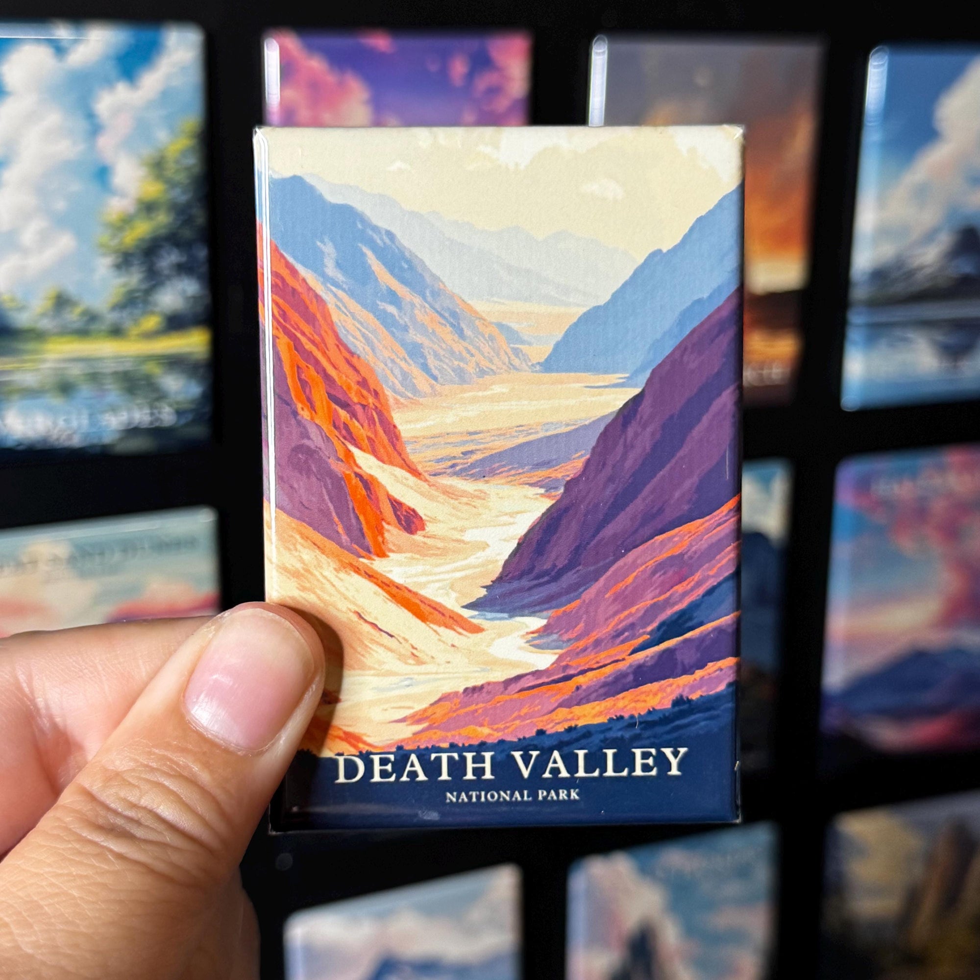 A hand holding a magnet with a colorful illustration of Death Valley National Park.