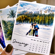 A hand holding a calendar with a photo of a couple in front of a snowy mountain landscape.
