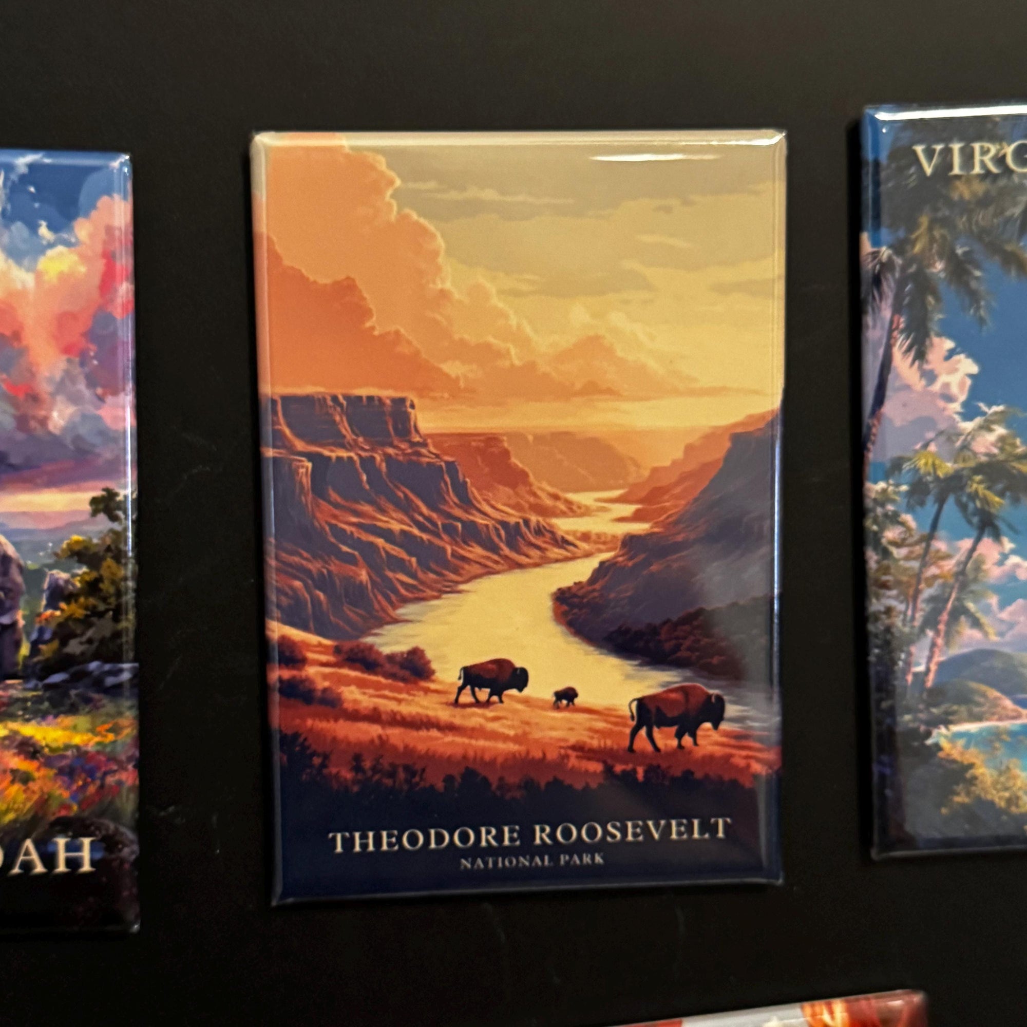 a magnet depicting a scenic landscape with a river, mountains, and wildlife, including two bison.