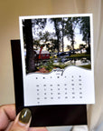 A person's hand holding a small calendar with a photo of a house and trees on the cover.